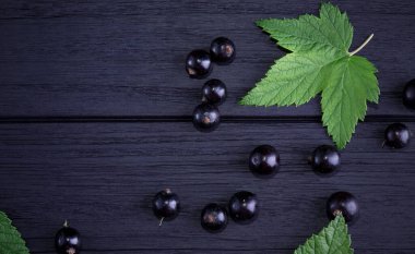 Siyah frenk üzümü ve koyu ahşap arka planda yeşil yapraklar. Frenk üzümü ve yeşil yapraklı arka plan. Frenk üzümü makrosu.