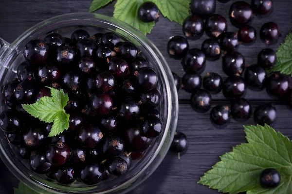 Black currant and green leaves on a dark wooden background. Background with currant berries and green leaves. Currant Macro.