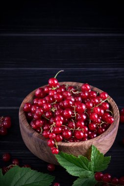 Koyu ahşap arka planda kırmızı frenk üzümü ve yeşil yapraklar. Frenk üzümü ve yeşil yapraklı arka plan. Frenk üzümü makrosu.