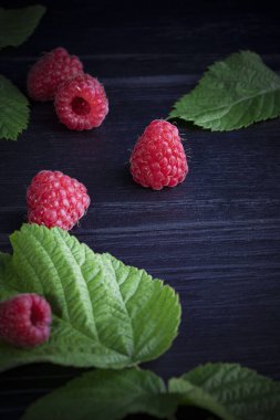 Koyu ahşap arka planda taze, kırmızı ahududular. Yeşil yapraklar. Metin için yer
