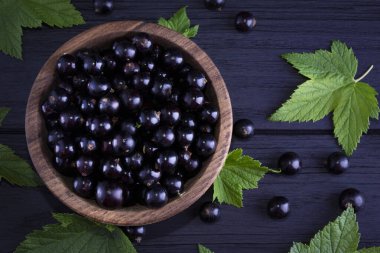 Siyah frenk üzümü ve koyu ahşap arka planda yeşil yapraklar. Frenk üzümü ve yeşil yapraklı arka plan. Frenk üzümü makrosu.