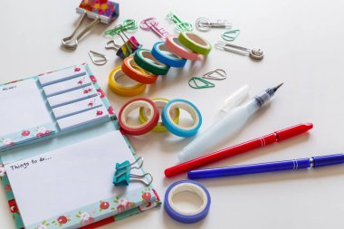 Stationery and details for work. Open notebook with colored paper clips, clip, scotch tape and fountain pen on a white background. Top view of the workplace.