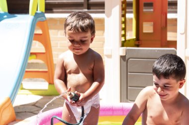 Mutlu kardeşler arka bahçedeki su hortumlarıyla oynarlar..