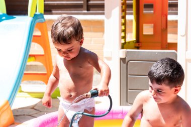 Mutlu kardeşler arka bahçedeki su hortumlarıyla oynarlar..