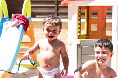 Mutlu kardeşler arka bahçedeki su hortumlarıyla oynarlar..