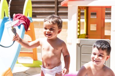 Mutlu kardeşler arka bahçedeki su hortumlarıyla oynarlar..