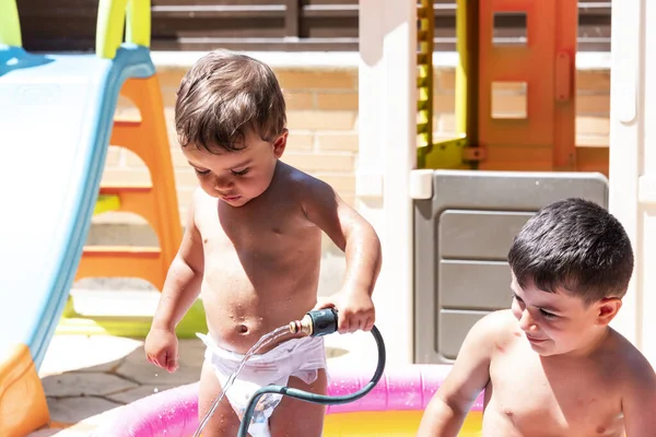 Mutlu kardeşler arka bahçedeki su hortumlarıyla oynarlar..