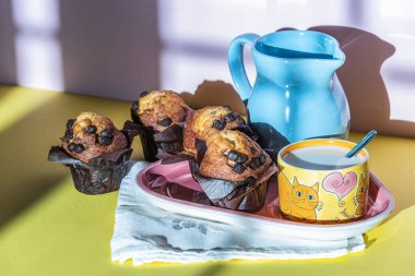 Süt ve kekle kahvaltı geleneksel bir çaydanlıkta servis edilir. Sarı ve pembe paletli..