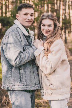 Çiftler kışın bir çam ormanında el ele tutuşup çerçeveye bakarlar.