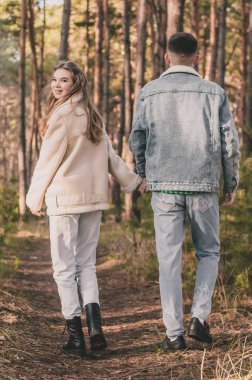 Bir çift tropiklerde çam ormanında yürürken bir adam bir kızın elini tutar ve o da çerçeveye bakar.