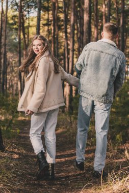 Bir çift tropiklerde çam ormanında yürürken bir adam bir kızın elini tutar ve o da çerçeveye bakar.
