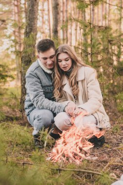 Bir çift kışın çam ormanında ateşin yanında ellerini ısıtır.