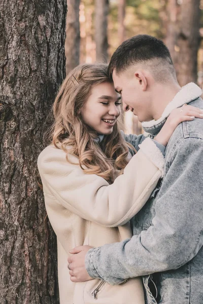 男は少女を木にもたせて抱きかかえ 松の森の中で微笑んだ — ストック写真
