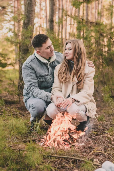 couple warms their hands near a fire in a pine forest in winter