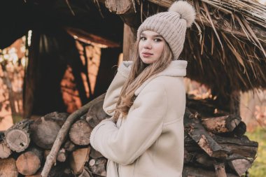 Kürk manto ve eldiven giymiş, katlanmış odunların arkasında poz veren ve gülümseyen güzel bir genç kız.