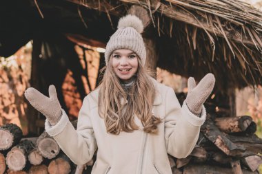 Kış kıyafetleri giymiş güzel bir genç kız eldiven giymiş elleri ve yakacak odunların arkasında kahkahalar atıyor.