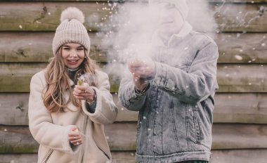 Kışın giyinmiş bir çift havai fişek patlatır ve ahşap bir çitin arkasında güler.