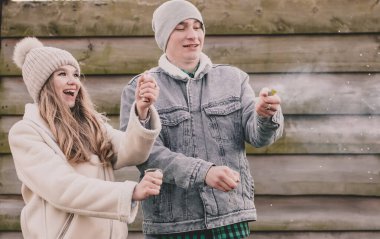 Kışın giyinmiş bir çift havai fişek patlatır ve ahşap bir çitin arkasında güler.