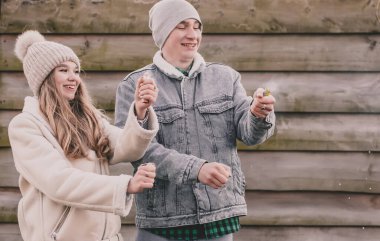 Kışın giyinmiş bir çift havai fişek patlatır ve ahşap bir çitin arkasında güler.