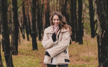 Uzun kıvırcık saçlı, uzun saçlı, güzel bir kadın model elinde kalp şeklinde bir Noel şekeri ve çam ormanındayken gülümsüyor.