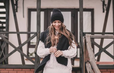 Manken görünümlü, uzun kıvırcık saçlı, kazaklı ve kürklü güzel bir kadın elinde maytapla beyaz bir evin arka planına gülümsüyor.