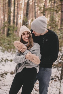 Bir adam bir kadına sarılır ve kadın çam ağacının arka planında gülümser.