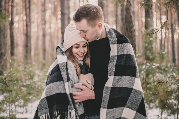 冬の松林を背景に毛布にくるまれキスをする男 — ストック写真