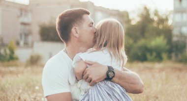 Baba küçük kızını kucaklıyor ve gülümsüyor.