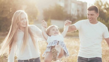Anne ve baba küçük kızla el ele tutuşup parkta daireler çiziyorlar.