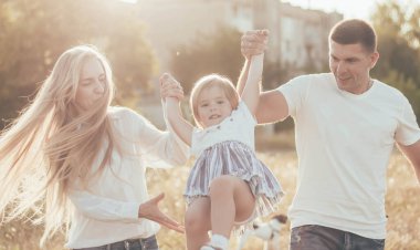 Anne ve baba küçük kızla el ele tutuşup parkta daireler çiziyorlar.