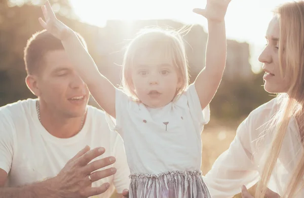 mom dad and daughter sit in the park on the grass and play