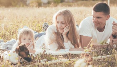 Anne, baba, kız ve köpek gün batımında çimlere uzanıyorlar.