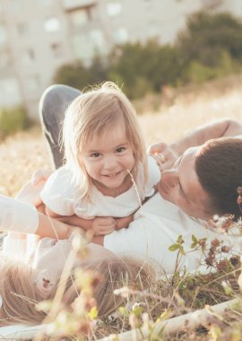 Anne, baba, kız ve köpek çimlere uzanıp oyun oynuyorlar.
