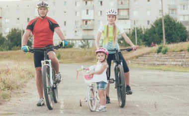 Anne, baba ve küçük kız stadyumda bisiklet sürüyorlar.