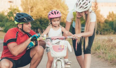 Annem ve babam küçük kızıma stadyumda bisiklet sürmeyi öğretiyorlar.
