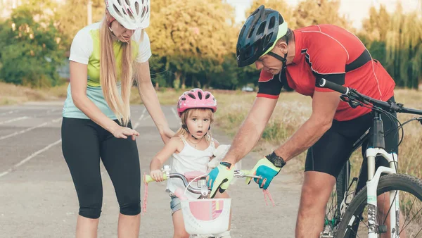 Mom and Dad are teaching little daughter to ride a bike in the stadium