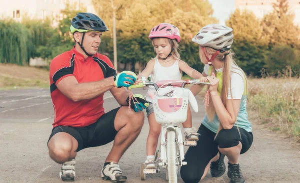 Mom and Dad are teaching little daughter to ride a bike in the stadium