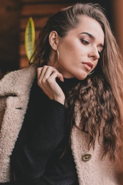 Uzun kıvırcık saçlı, manken görünümlü bir kadın restoranda oturur ve pencereden dışarı bakar.