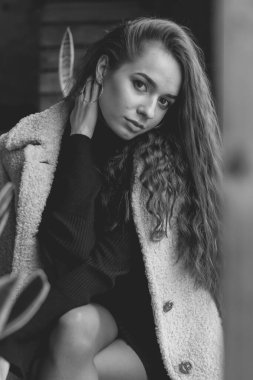 Uzun kıvırcık saçlı, manken görünümlü bir kadın restoranda oturur ve pencereden siyah beyaz fotoğrafa bakar.