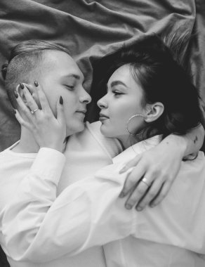 Evde giysileri içinde bir çift yatakta uzanıp birbirlerine sarılıyorlar. Siyah beyaz fotoğraf.