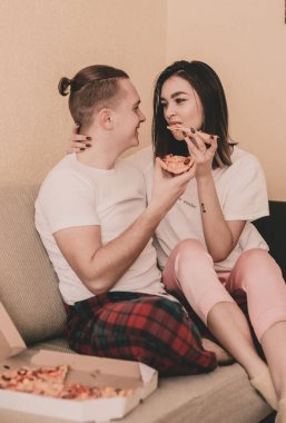 Evde kıyafetlerini giyip evde pizza yiyen bir çift.