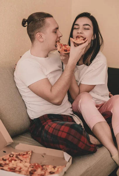 穿着家居服躺在床上吃披萨的夫妻 — 图库照片