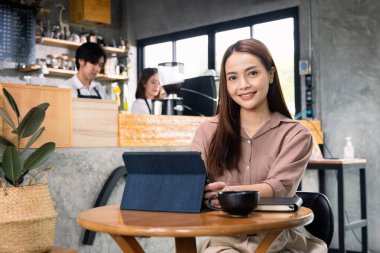 Tabletle çalışan genç ve güzel bir iş kadını kafeteryada oturuyor..