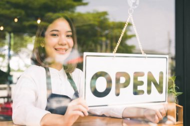 Genç Asyalı kız müşteriyi karşılamak ve sabah kahve dükkanı açmak için açık etiketi çevir. Dişi Asyalı Barista aynadaki yansımayla kapının önündeki kahve kafesini açıyor..