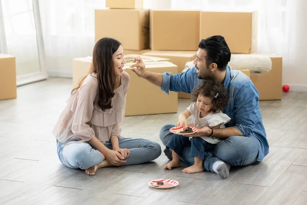 Happy moment family eating chocolate cookie in living room at home. Father Mother and daughter laughing having a good meal in the morning.