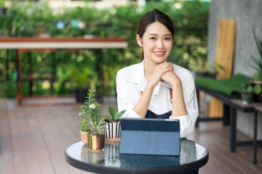 Ev bitkilerinde çalışan Asyalı genç ve tatlı bir kadın. Asyalı kadın bahçıvan, seradaki ağaçların büyümesini kaydetmek ve yakalamak için tablet kullanıyor. Ev konseptinden küçük işletme çalışmaları başlat.