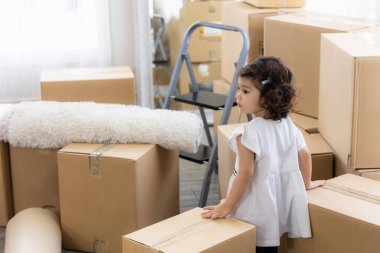 Evde tatlı bir kız var. Aile yeni taşınıyor. Yerde bir sürü paket var..