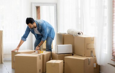 Genç adam yeni bir eve taşınıyor. Paketleri açıyor ve oturma odasının zeminini düzenliyor..