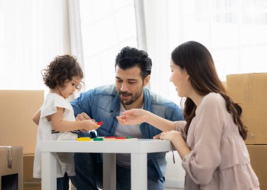 Ebeveynler ve kızları evdeki oturma odasında yerde oturan tahta bloklarla oynuyorlar. Aile yeni bir eve taşındı. Mutlu an. Çok ırklı baba, anne ve çocuk..