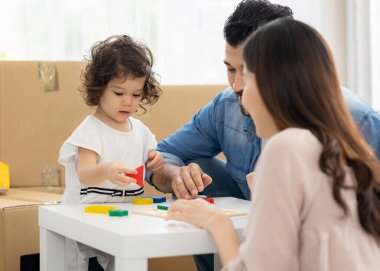 Ebeveynler ve kızları evdeki oturma odasında yerde oturan tahta bloklarla oynuyorlar. Aile yeni bir eve taşındı. Mutlu an. Çok ırklı baba, anne ve çocuk..